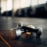 Athletes training on shock-absorbing rubber gym flooring with free weights and exercise equipment in a modern fitness facility.