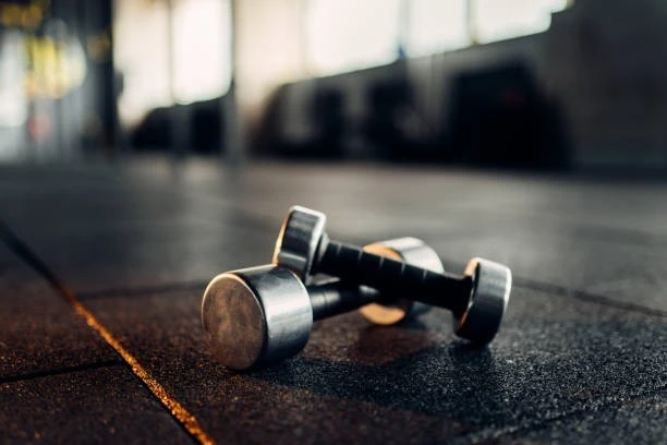 Athletes training on shock-absorbing rubber gym flooring with free weights and exercise equipment in a modern fitness facility.