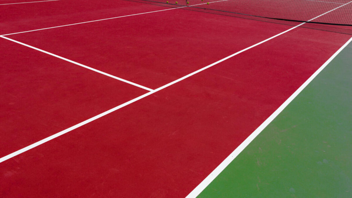 Outdoor tennis court with visible surface cracks and worn coating caused by weather, moisture, and heavy use.