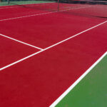 Outdoor tennis court with visible surface cracks and worn coating caused by weather, moisture, and heavy use.