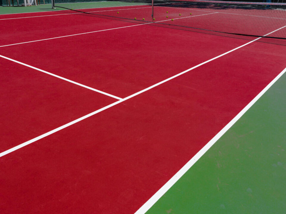 Outdoor tennis court with visible surface cracks and worn coating caused by weather, moisture, and heavy use.