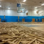 Indoor hardwood basketball court undergoing professional inspection to determine whether repair, refinishing, or full floor replacement is needed.