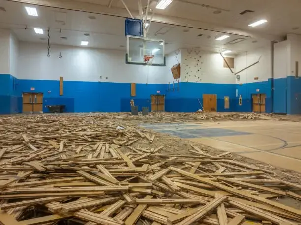 Indoor hardwood basketball court undergoing professional inspection to determine whether repair, refinishing, or full floor replacement is needed.