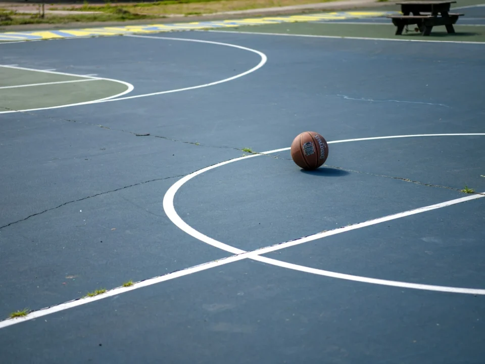 Indoor hardwood basketball court with surface scratches and worn finish restored through professional hardwood gym floor refinishing.